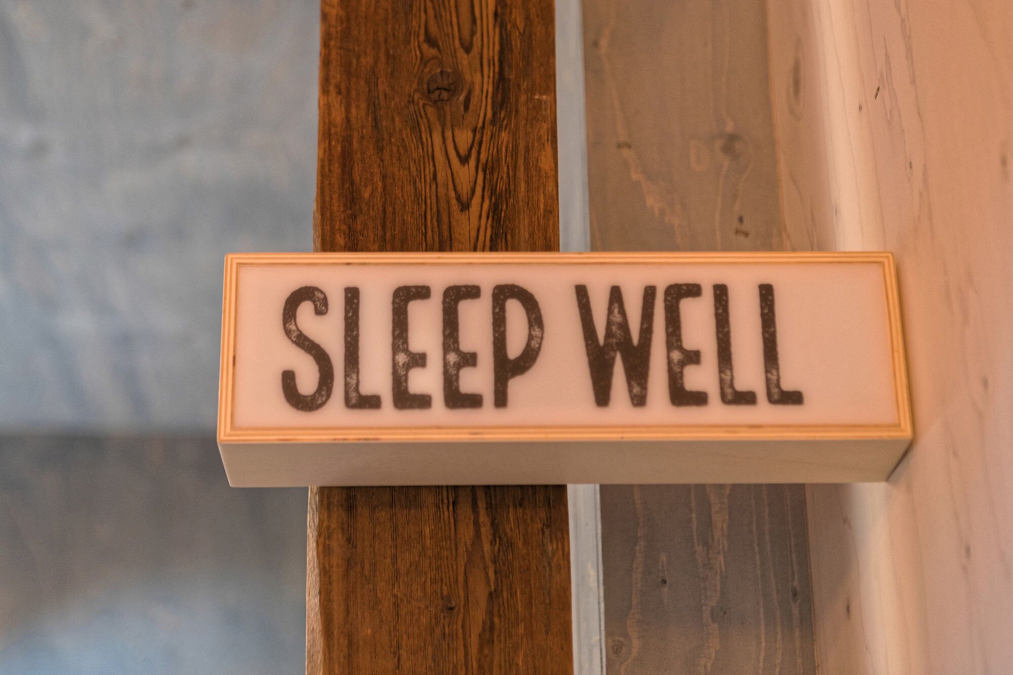 A wooden sign with the text "SLEEP WELL" mounted on a wall.