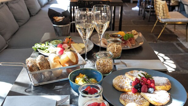 A dining table with various dishes, including bread, fruit, and desserts, and two glasses of white wine. - Alter Schlachthof (Bressanone)