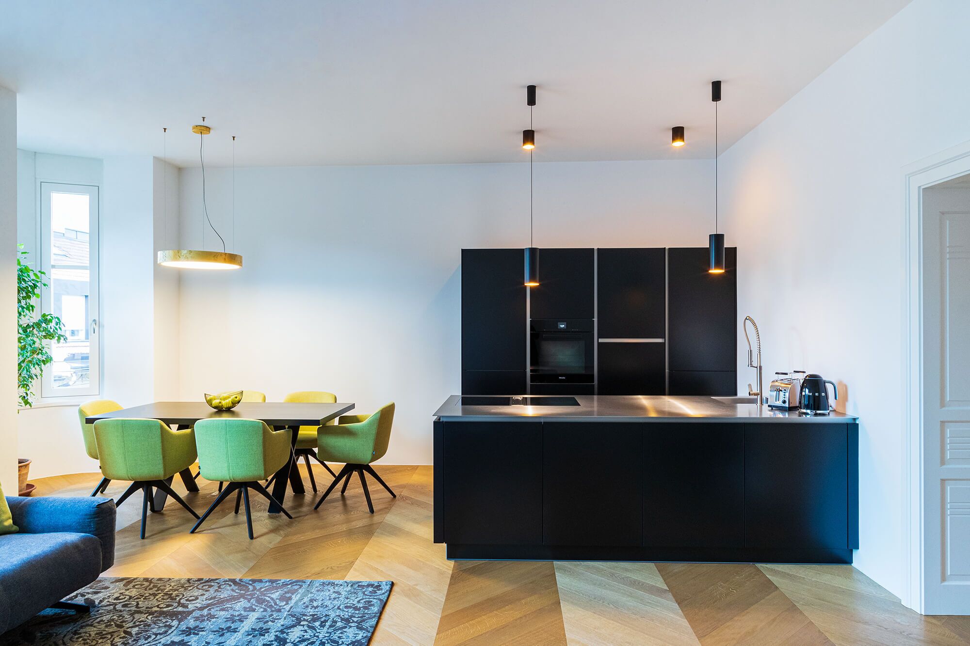 A modern kitchen with a central island, black cabinetry, and a dining area with green chairs.