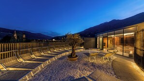 A rooftop terrace with lounge chairs, a potted tree, and a modern building with glass walls. - Alter Schlachthof (Bressanone)