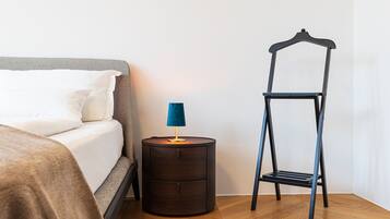 Un dormitorio con una cama, una mesita de noche con lámpara y una estantería metálica.