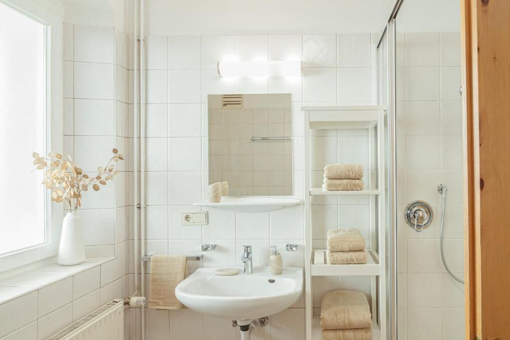 Ein modernes Badezimmer mit einem weißen Waschbecken, Spiegel und Regalen mit Handtüchern.