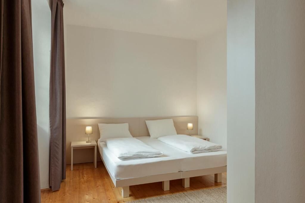 A bedroom with a double bed, two bedside tables with lamps, and a wooden floor.
