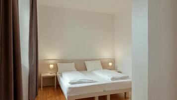 A bedroom with a double bed, two bedside tables with lamps, and a wooden floor.