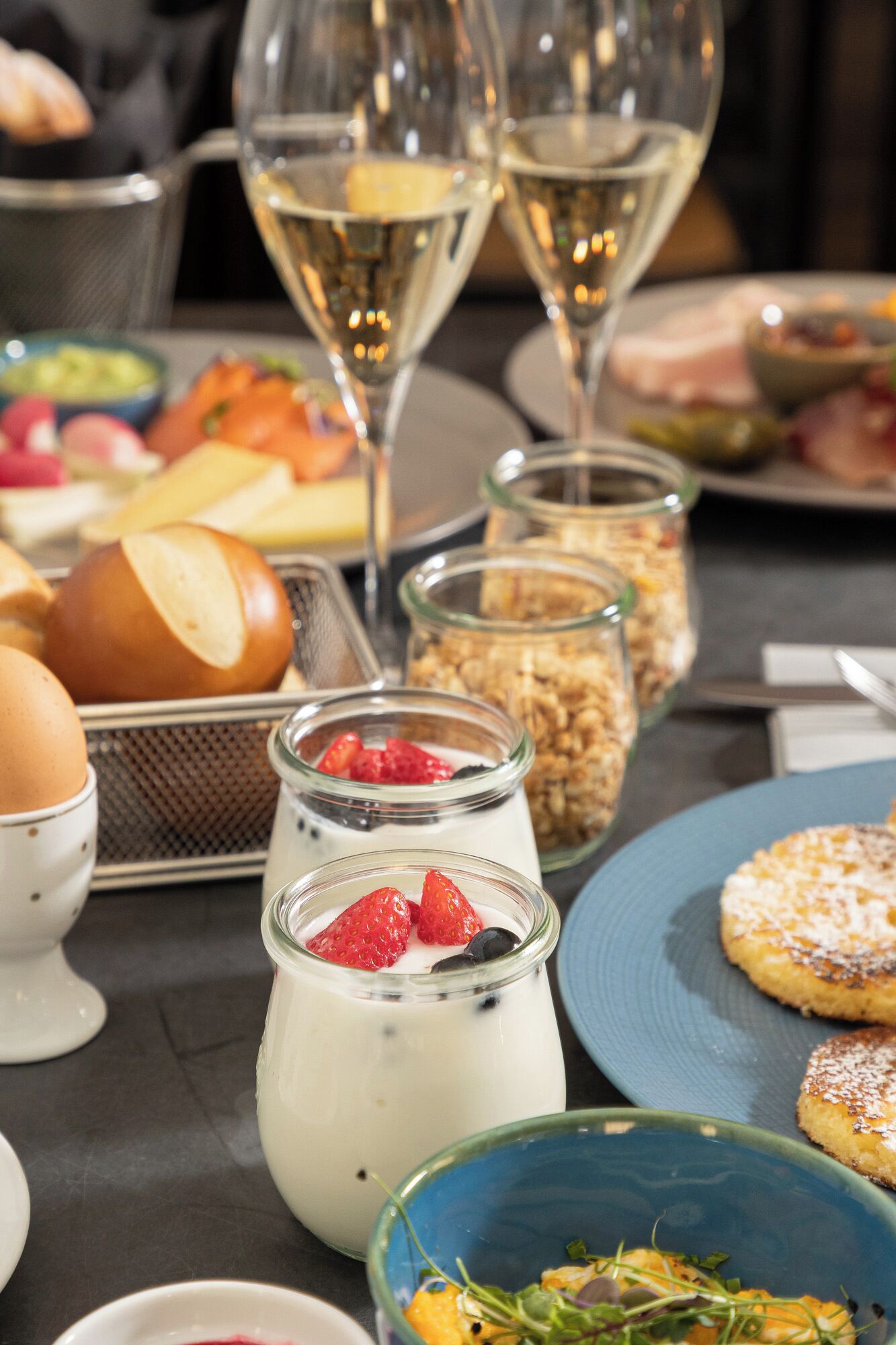 A table with various food items, including yogurt with strawberries, bread, and a blue plate with pastries.