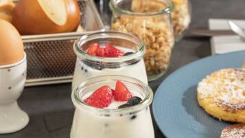 A table with various food items, including yogurt with strawberries, bread, and a blue plate with pastries.
