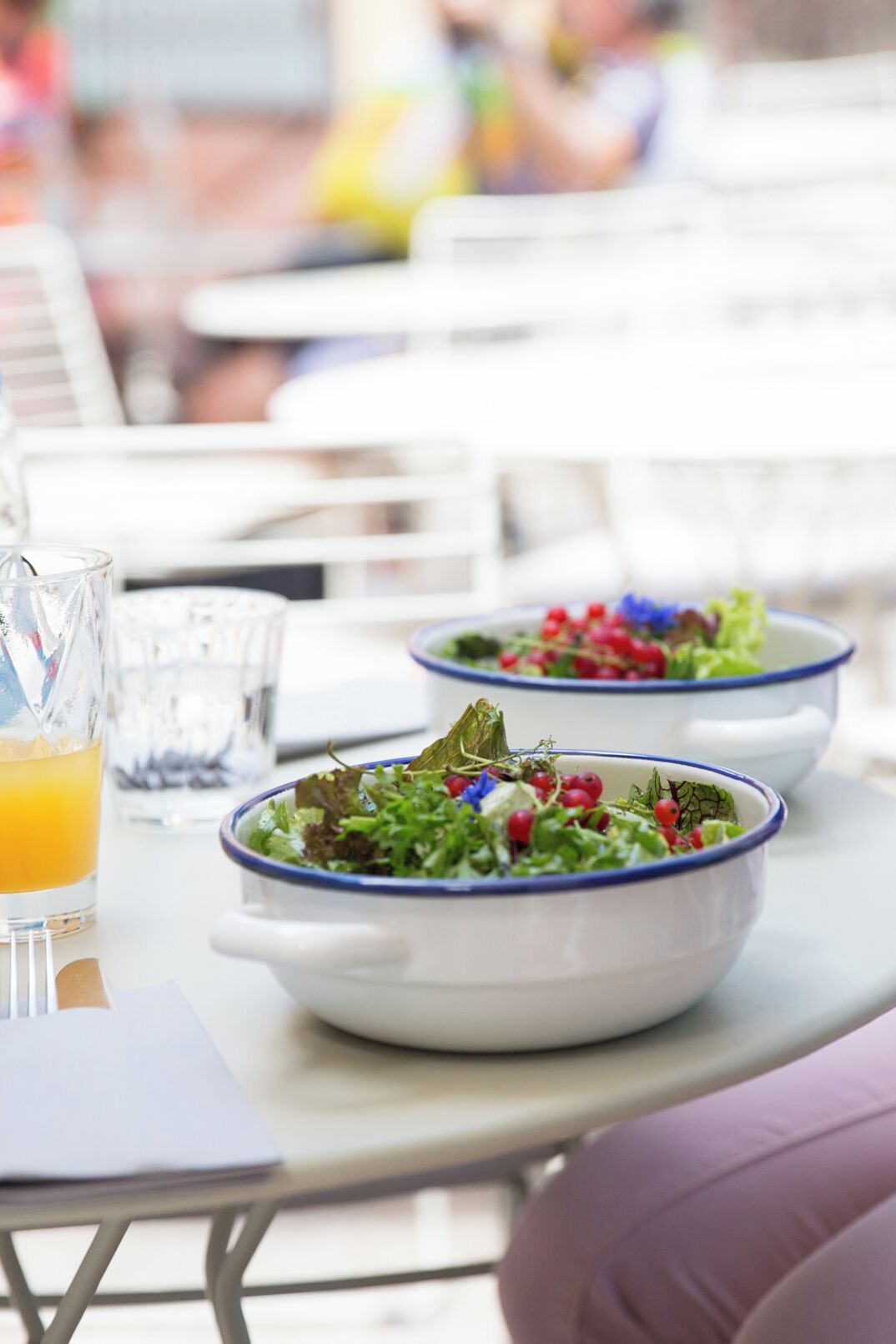 Una mesa con dos tazones blancos que contienen una ensalada, un vaso de jugo de naranja y una servilleta.