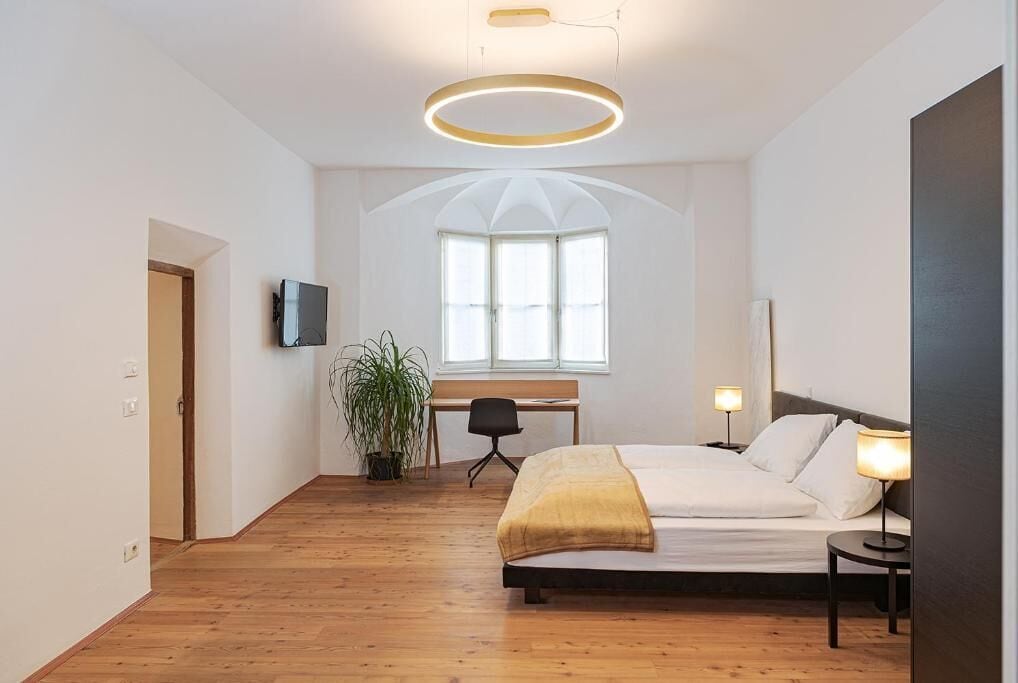 A modern bedroom with a large bed, a desk, a chair, and a TV.