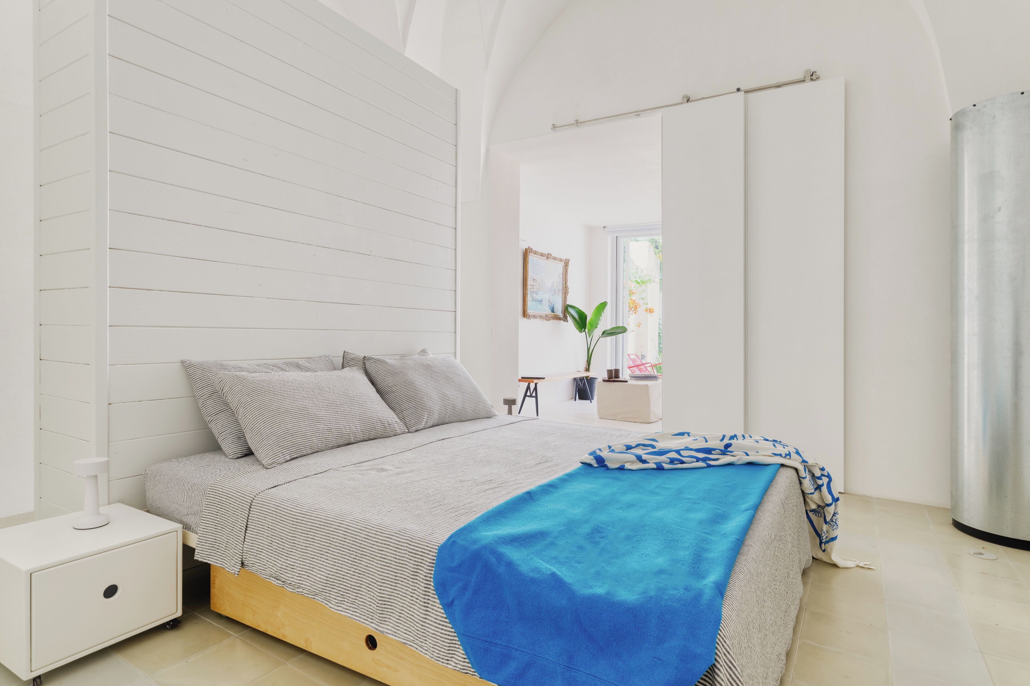 Ein Schlafzimmer mit einem Bett, einem Nachttisch, einer Topfpflanze und einem Fenster.