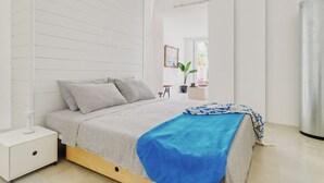 Un dormitorio con cama, mesita de noche, planta en maceta y ventana.