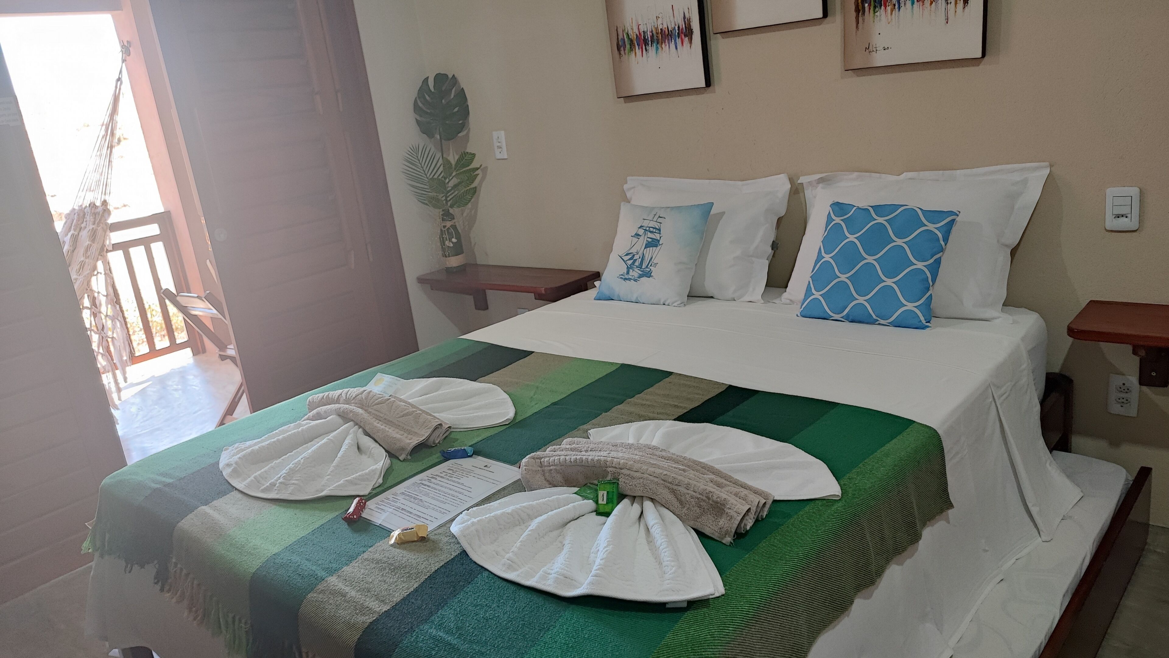A neatly made bed with towels, a green and white striped bedspread, and a sailboat pillow. There is a small plant on a nightstand beside the bed.