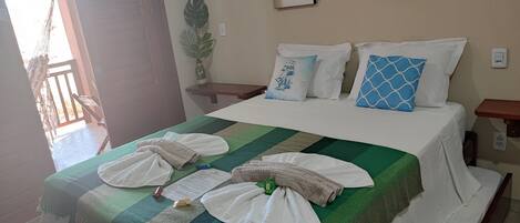 A neatly made bed with towels, a green and white striped bedspread, and a sailboat pillow. There is a small plant on a nightstand beside the bed.