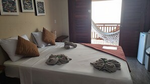 A neatly made bed with towels, pillows, and a blanket in a room with a balcony and a hammock. - Pousada Areias de Flecheiras (Trairi)