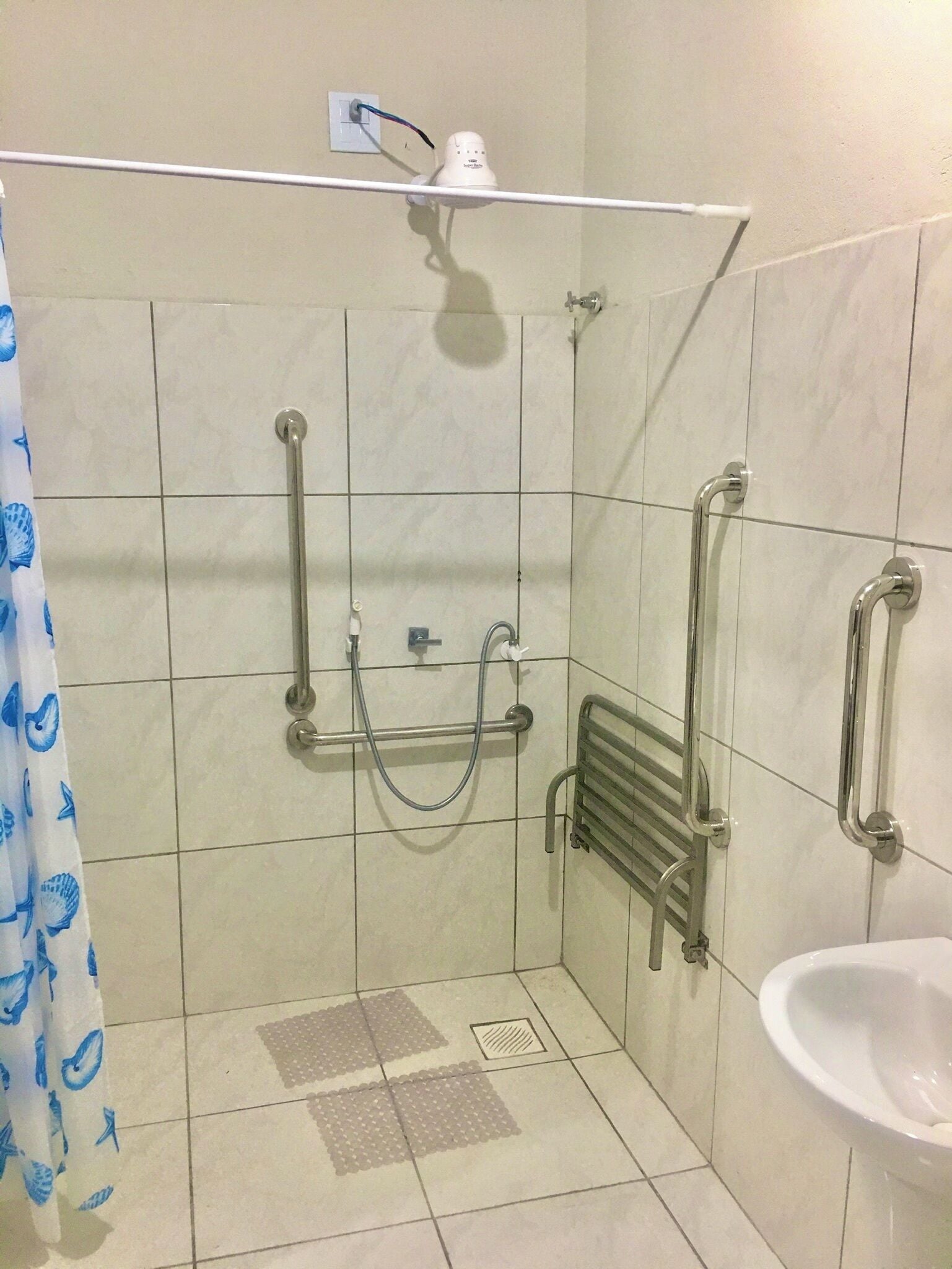 A bathroom with a shower, grab bars, a hand dryer, and a sink.