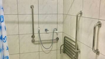 A bathroom with a shower, grab bars, a hand dryer, and a sink.