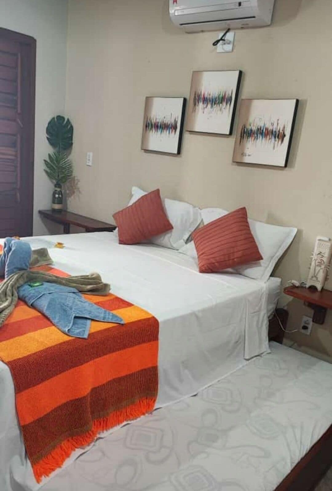Quarto de hotel com uma cama, mesa de cabeceira, ar condicionado e obras de arte na parede.