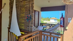 A balcony with a hammock, wooden railing, and a view of a building and trees. - Pousada Areias de Flecheiras (Trairi)