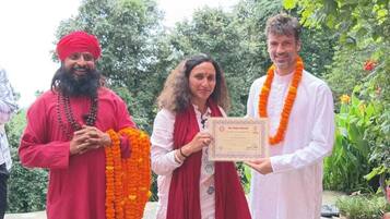 Three individuals holding a framed certificate outdoors with greenery in the background.