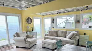 A spacious living room with a large window overlooking the sea, a cozy sofa set, a dining table with chairs, and a ceiling fan. - Sunsets over Long Island Sound Peace and Tranquility 
Monthly Rentals Available  (Calverton)
