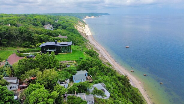 An aerial view of a coastal property with multiple houses, a large modern house with a glass facade, and a beach with clear water. - Sunsets over Long Island Sound Peace and Tranquility 
Monthly Rentals Available  (Calverton)