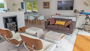 A modern living room with a fireplace, a sofa, a dining area, and a large TV. - 3 bedroom accommodation in Bonawe (Bonawe)