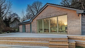 A modern house with a wooden exterior, large glass sliding doors, and a wooden deck. - 3 bedroom accommodation in Bonawe (Bonawe)