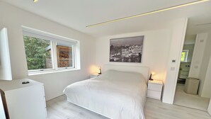 A modern bedroom with a large bed, bedside tables, a window with a view of greenery, and a cityscape painting on the wall. - 3 bedroom accommodation in Bonawe (Bonawe)