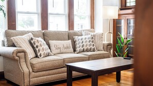 Un salón con un sofá seccional color beige, una mesa de centro de madera y un ventanal con persianas.