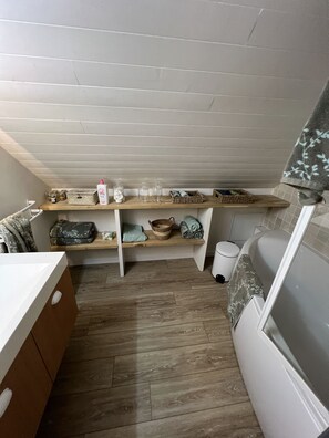 Ein kleines Badezimmer mit Holzboden, einer weißen Badewanne und einem Ablagefach mit Pflegeprodukten und einem Korb.