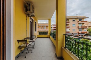 A balcony with a table and chairs, air conditioning unit, and a view of neighboring buildings.