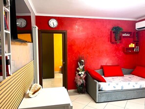 A modern living room with a red accent wall, a sofa with red cushions, a white table, and a clock on the wall.