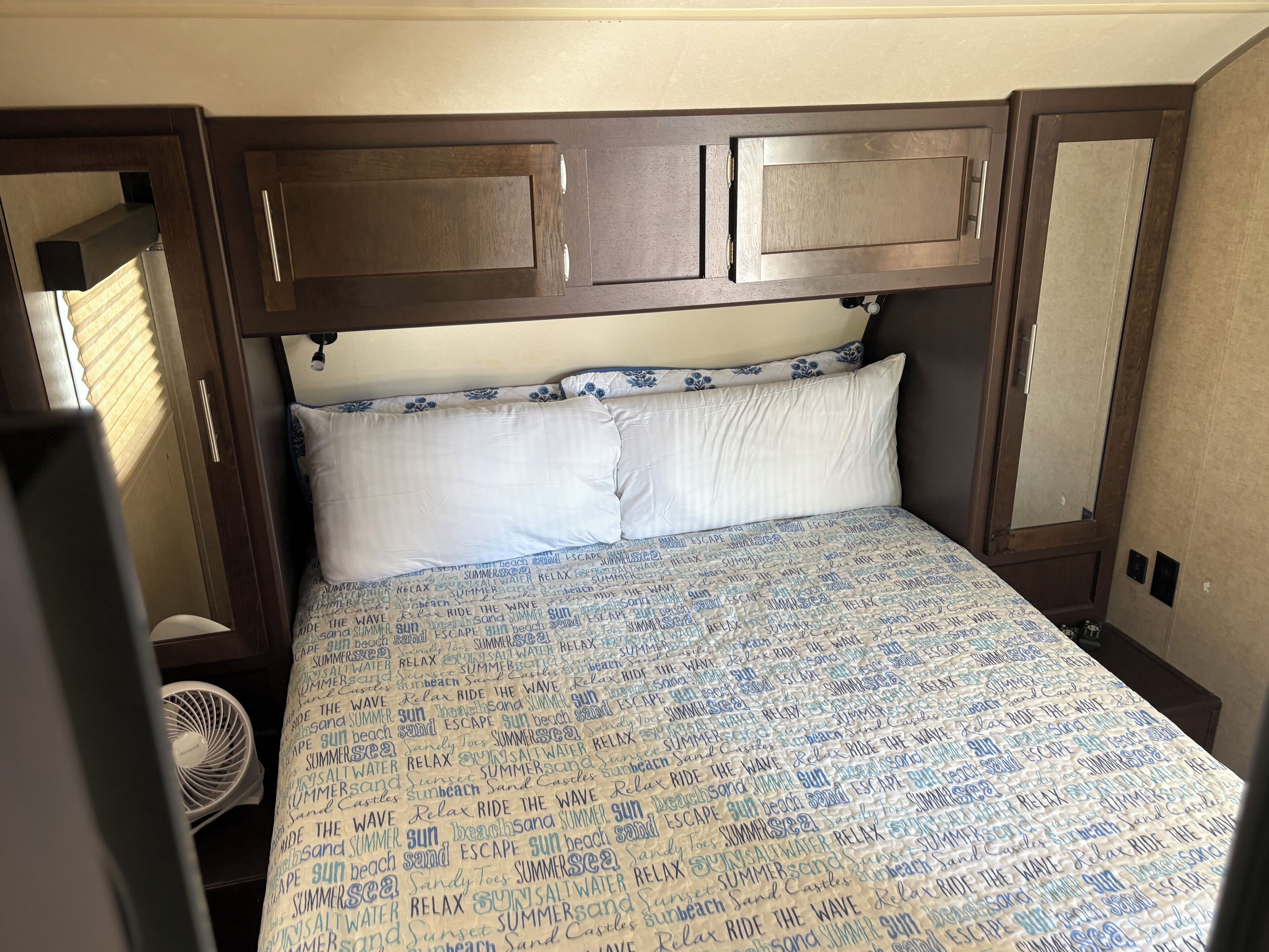 Een slaapkamer met een bed, een ventilator en houten kasten erboven.