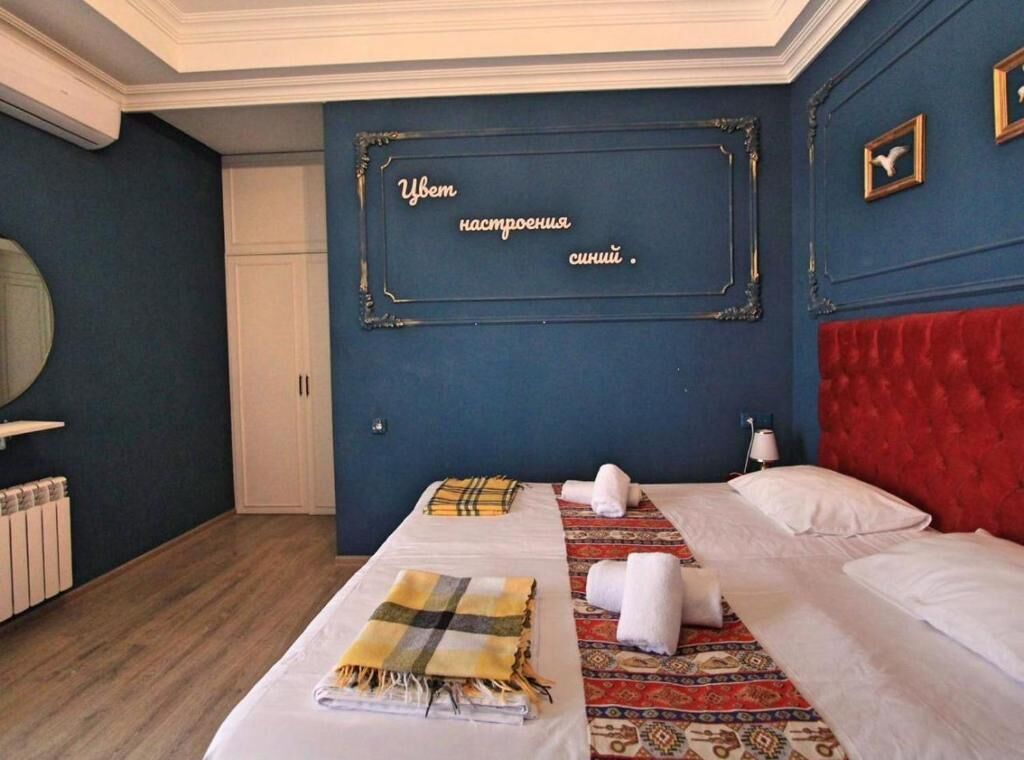 Habitación de hotel con cama, cabecera roja, espejo de pared y una placa decorativa.