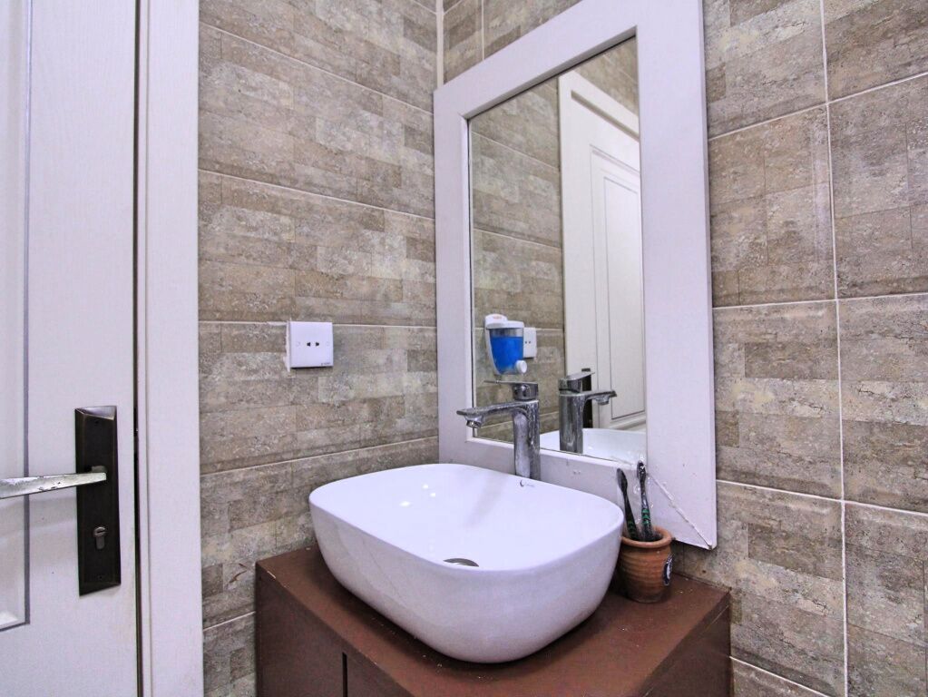 Un baño con un lavamanos blanco, un espejo y una pared con azulejos.