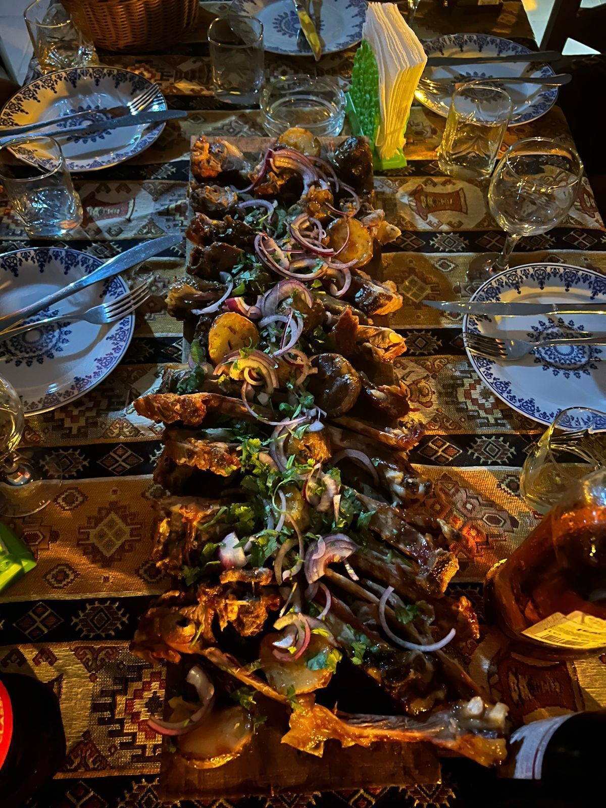 A dining table set with plates, cutlery, and a large dish of food garnished with onions and herbs.