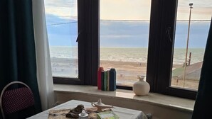 A room with a table set for two, a view of the sea, and a window with curtains. - NovART Gallery&Sea Hotel (Sumqayit)