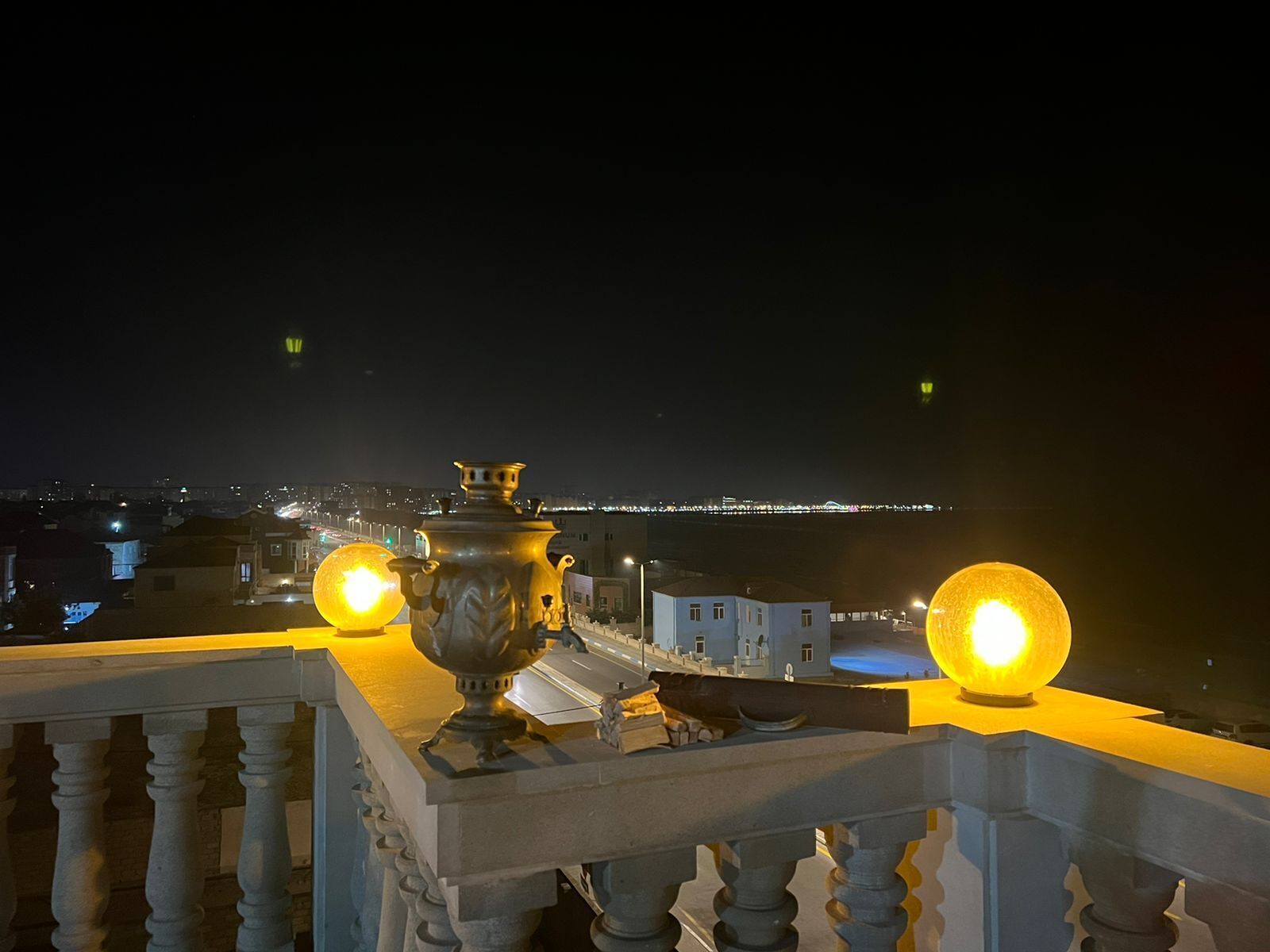 A balcony with a decorative urn and two spherical lights, overlooking a cityscape at night.