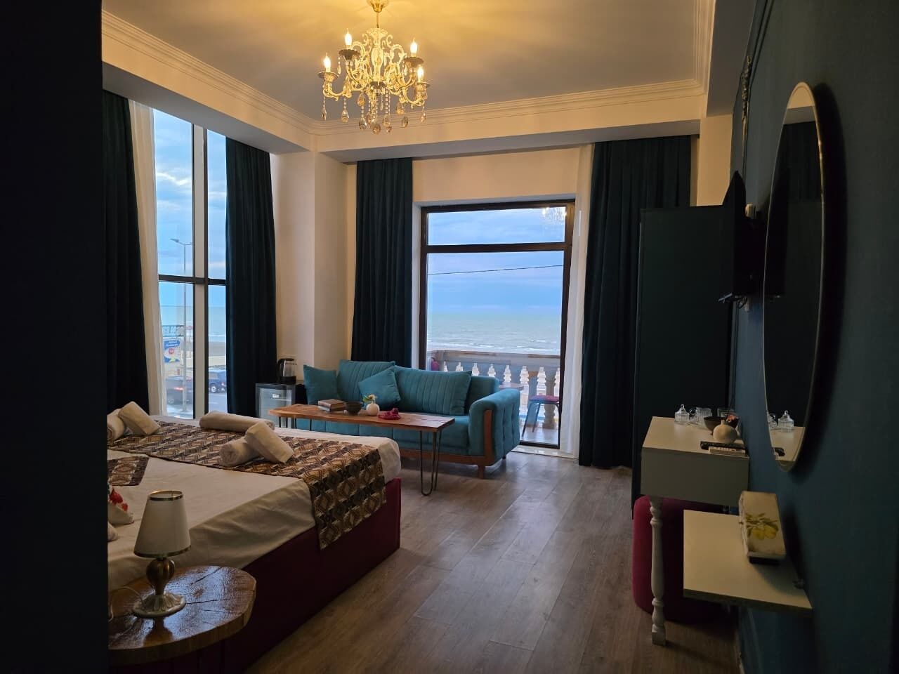 A hotel room with a bed, a sofa, a table, a mirror, and a view of the sea.