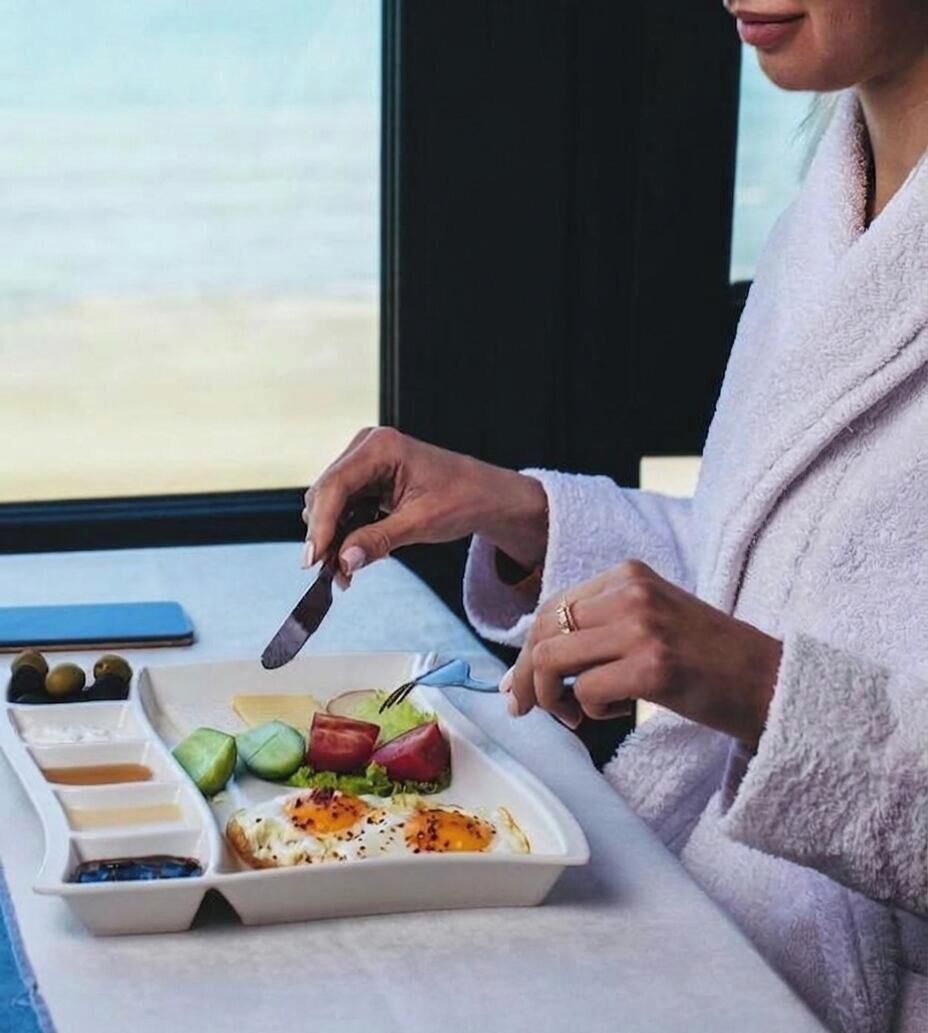Une personne vêtue d’une robe découpe des aliments sur un plateau, parmi lesquels on peut distinguer des œufs, des légumes verts et de la viande.