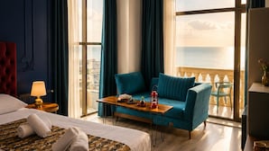 A hotel room with a bed, a sofa, a table with items, a chandelier, and a view of the sea. - NovART Gallery&Sea Hotel (Sumqayit)