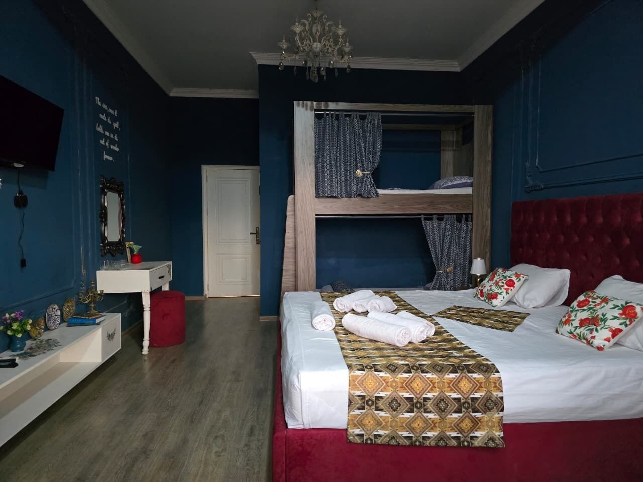 Ein Schlafzimmer mit Etagenbett, Nachttisch, Spiegel und einem roten, mit Stoff bezogenen Kopfteil.