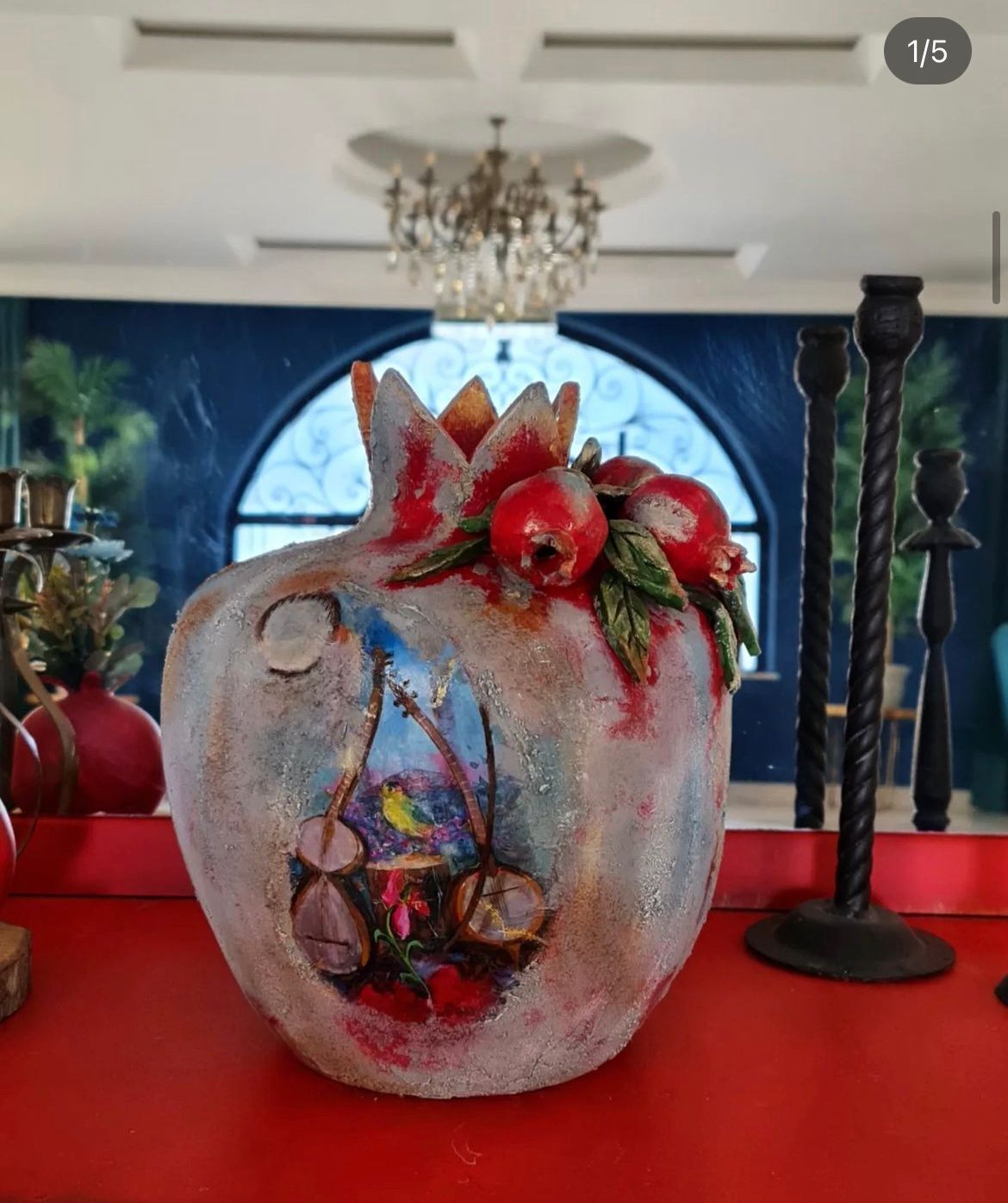 Une grenade ornée de motifs peints, un lustre et, en arrière-plan, une fenêtre bleue en arc de cercle.