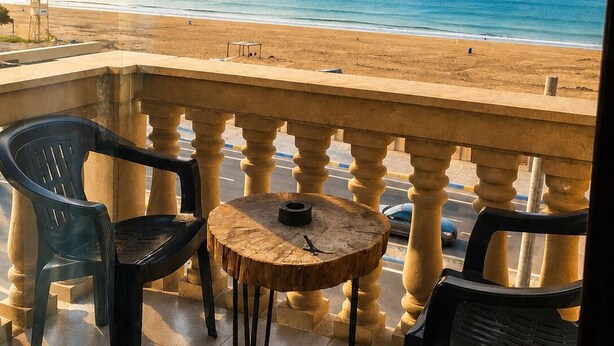 A balcony with a view of the beach, a round wooden table, and two plastic chairs. - NovART Gallery&Sea Hotel (Sumqayit)