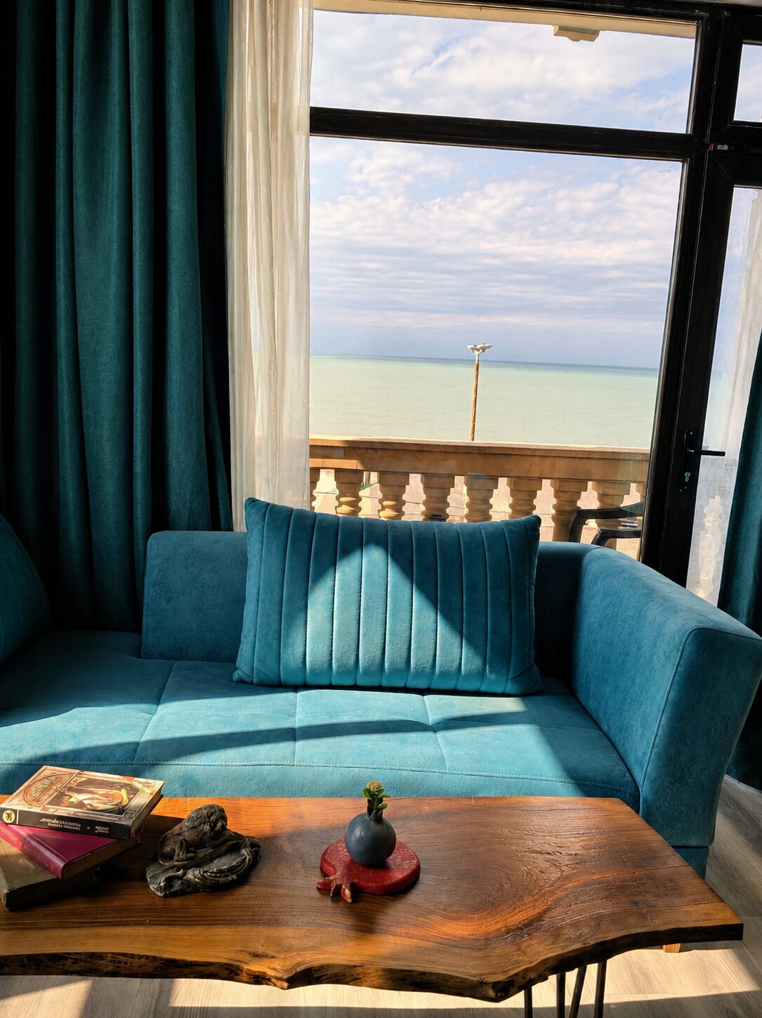 A room with a sofa facing a balcony with a view of the sea.