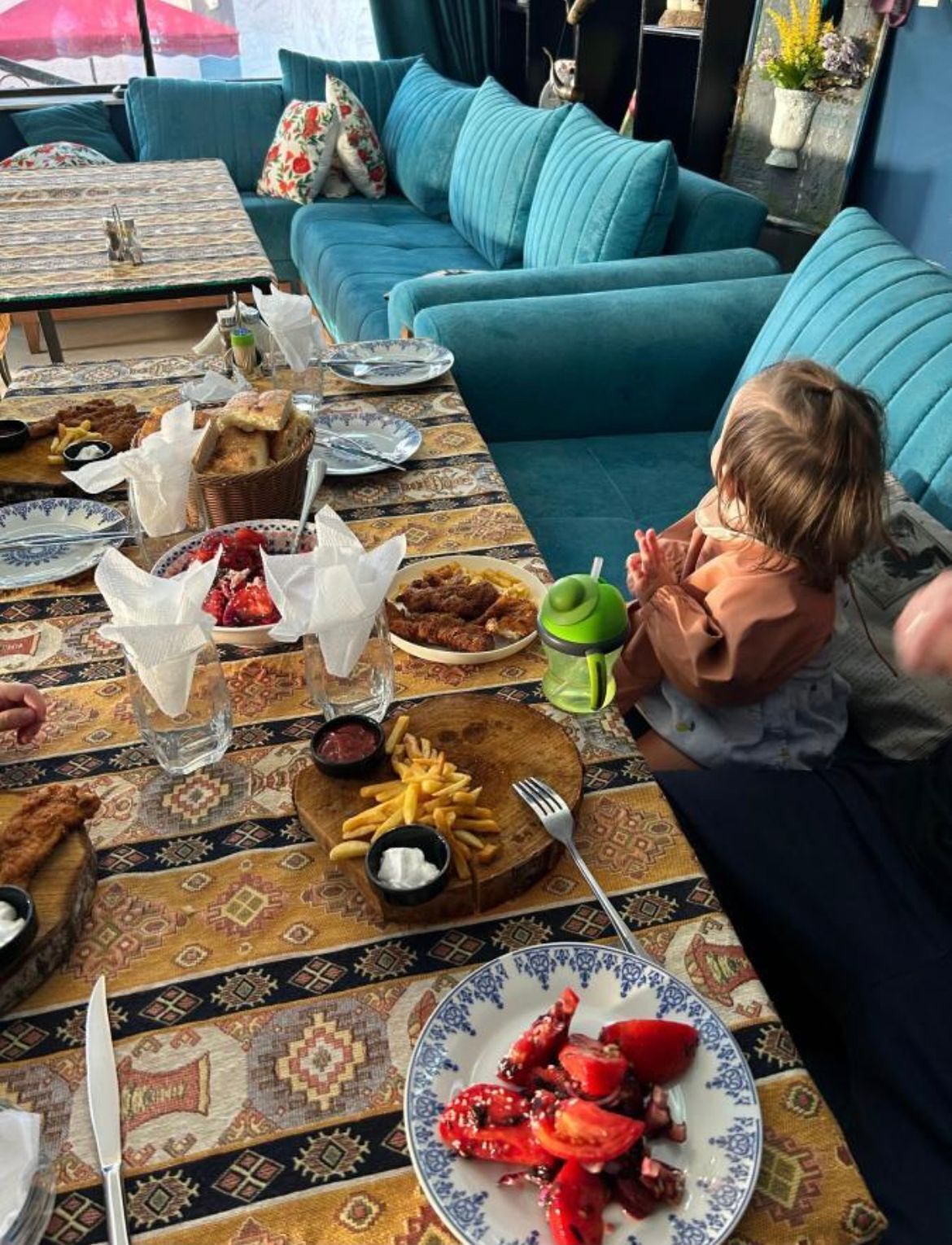 A dining table with a variety of dishes, including a plate of red tomatoes, a basket of bread, and a green mug.