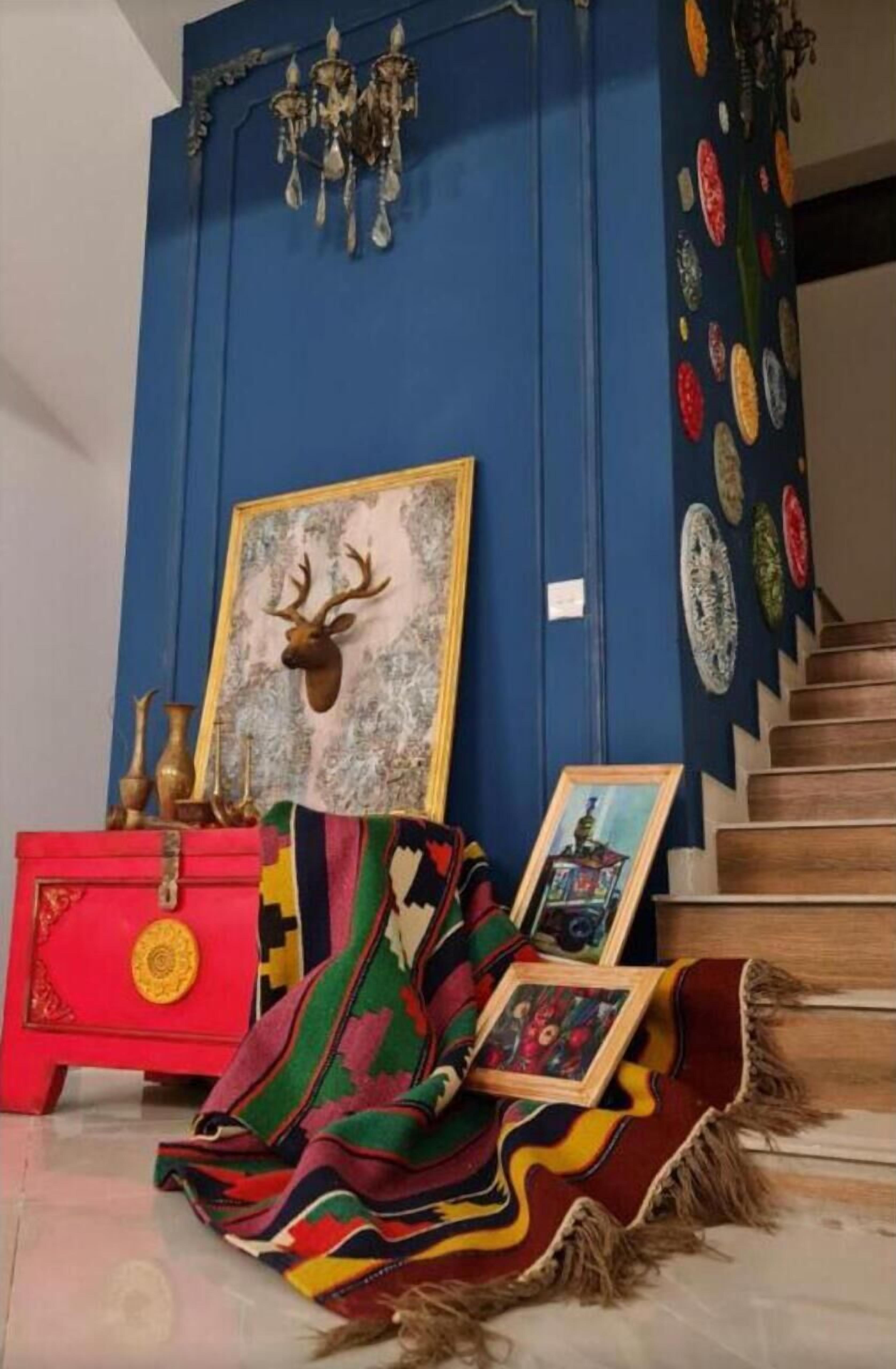 Een kamer met een blauwe wand, een rode dressoir, een kamerkleed met patroon en een hertenkop in een lijst.