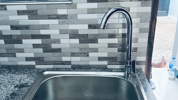 A kitchen with a stainless steel sink, granite countertop, and a tiled backsplash. - OSIM HOMES (Arusha)