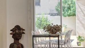 A room with a dining table, chairs, a decorative statue, and a view through a large window.