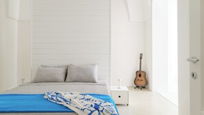 A bedroom with a bed, pillows, a blanket, a guitar, and a bedside table.