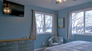 A bedroom with a bed, a dresser, a chair, and two windows.